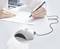 A hand is writing with a pen on a form; the pen is connected by a chain to a white holder.