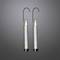 Two elegant, slender candles in clear glass cylinders on curved, black holders, glowing against a grey background.