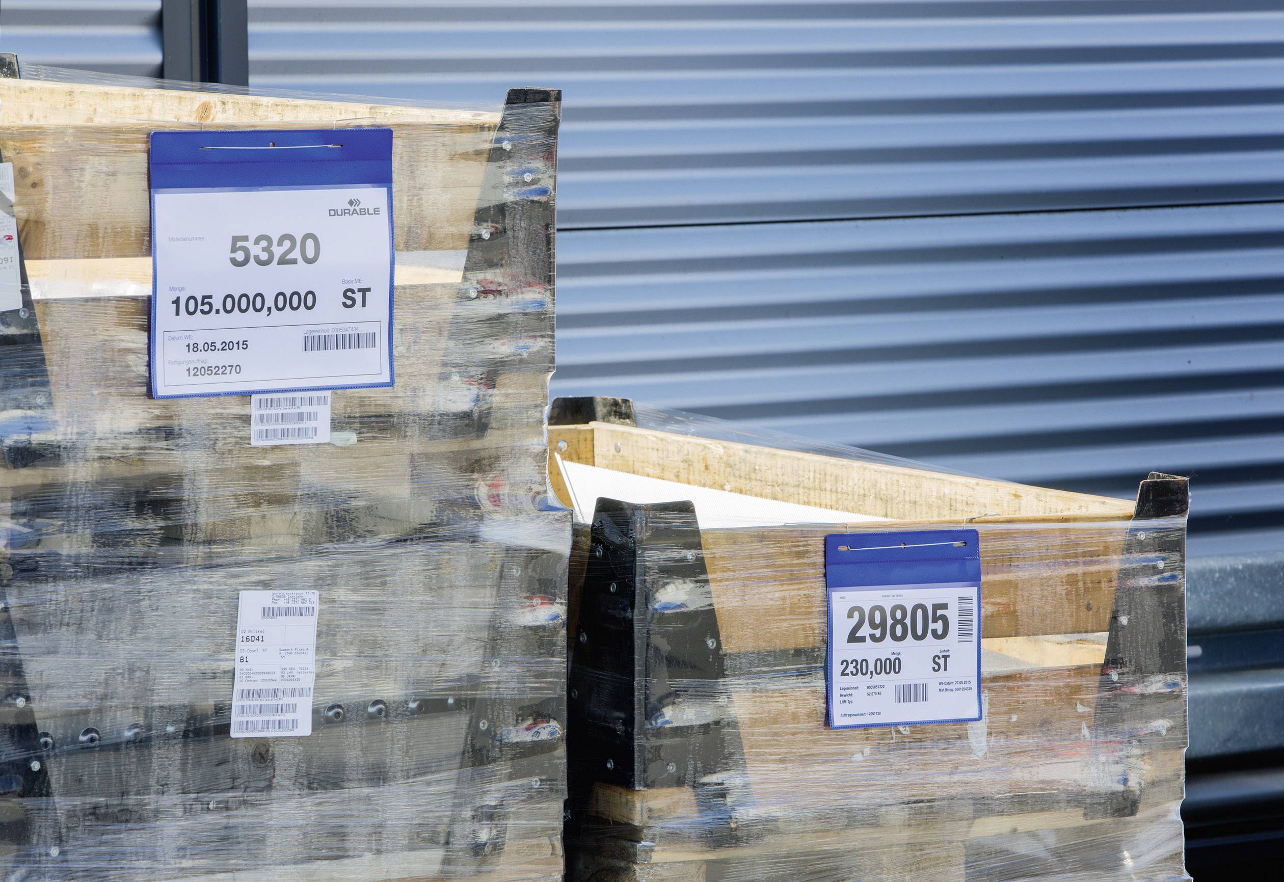 Two wooden pallets in front of a building. Stickers display numbers: '5320' and '29805' with quantity specifications.