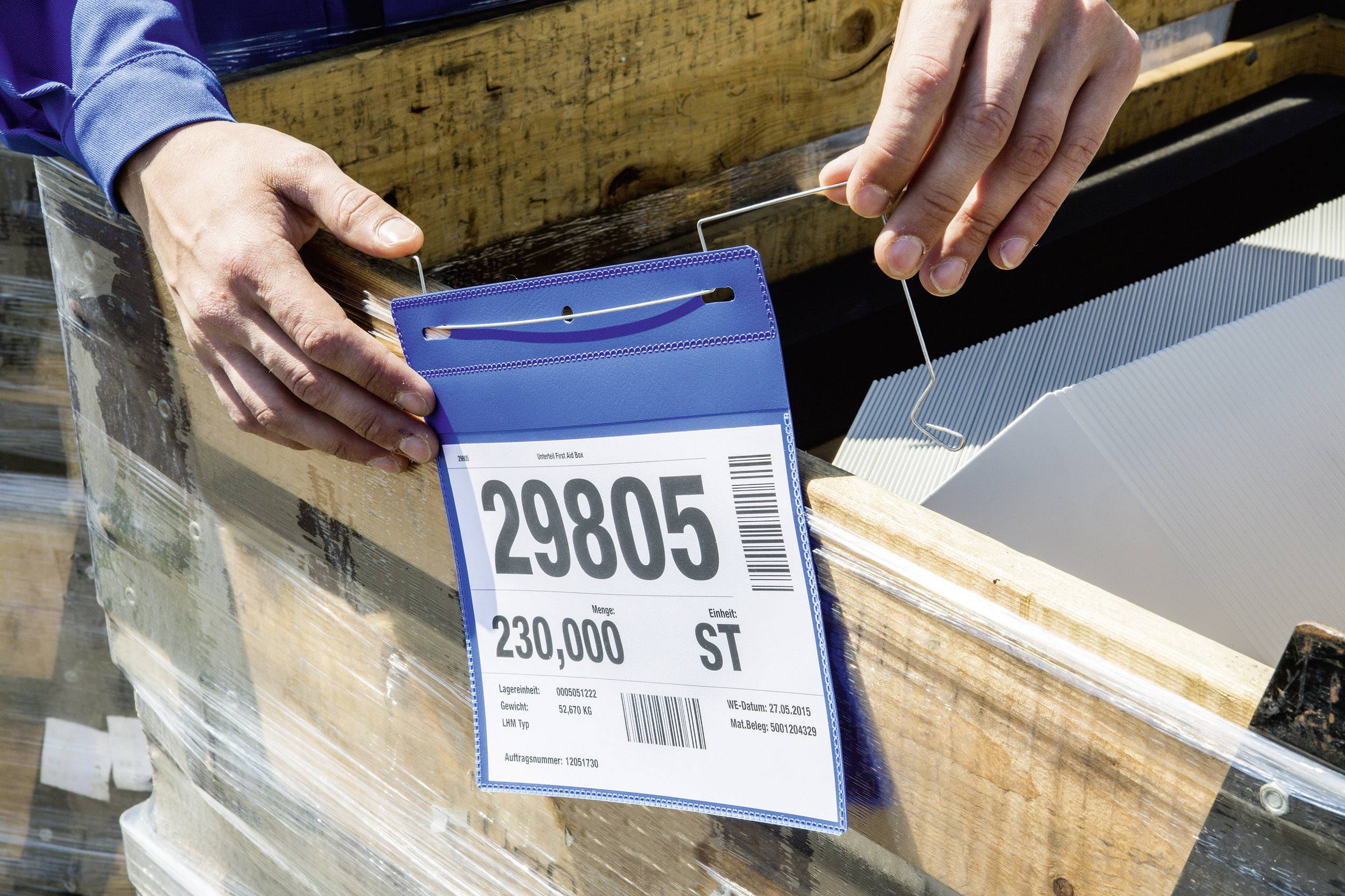 A person is holding a sign with the number '29805' and the text '230,000 ST', attached to a wooden box.