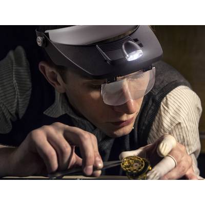 A person is working intently on a small, mechanical object, wearing a magnifying glasses with built-in light.