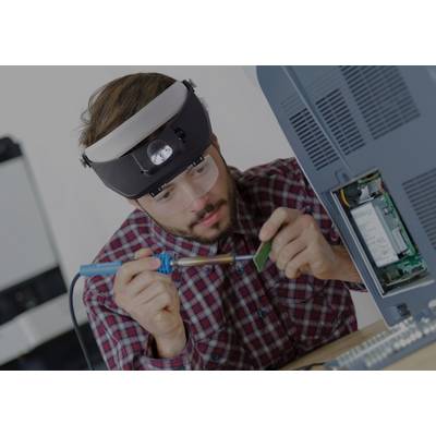 A man is soldering intently on a circuit board inside a computer case. He is wearing safety glasses and a magnifying visor.