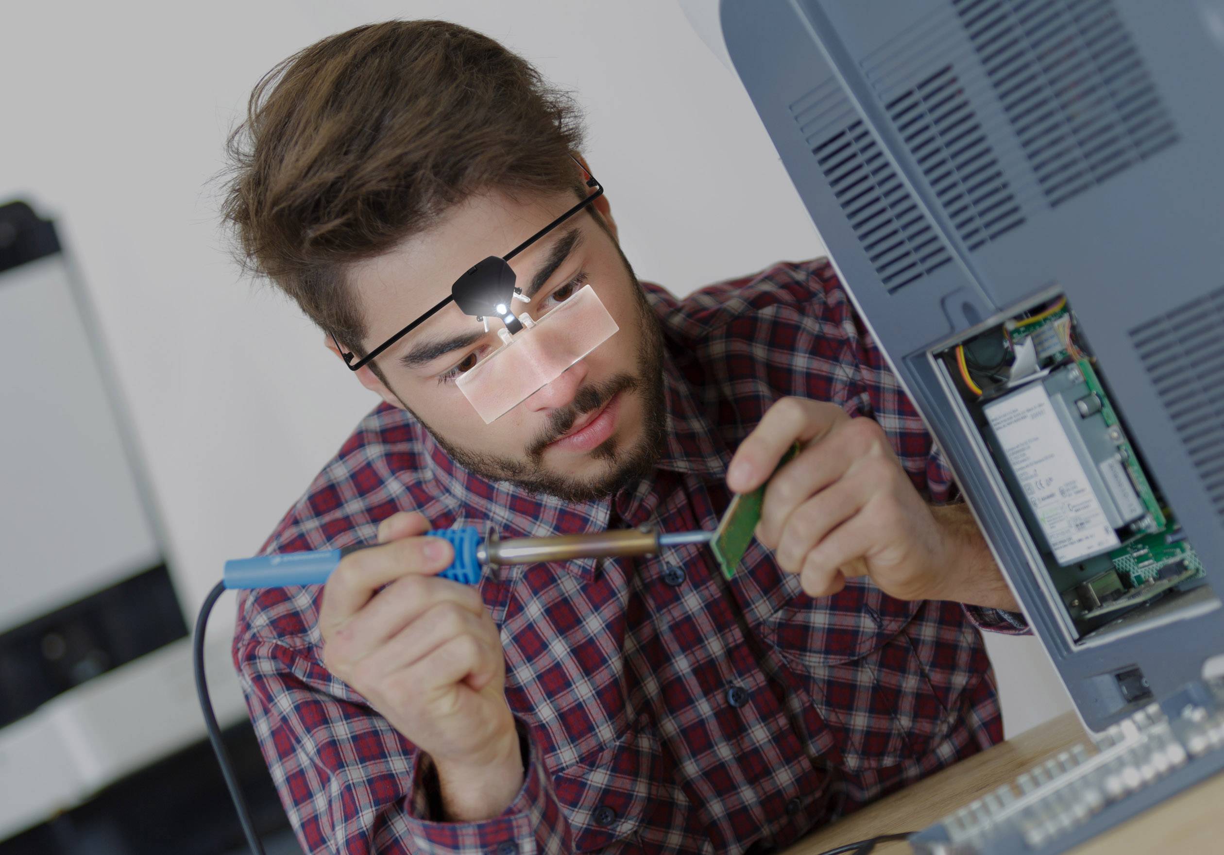 A person is soldering an electronic component on an open housing unit. They are wearing a head torch and have a concentrated gaze.