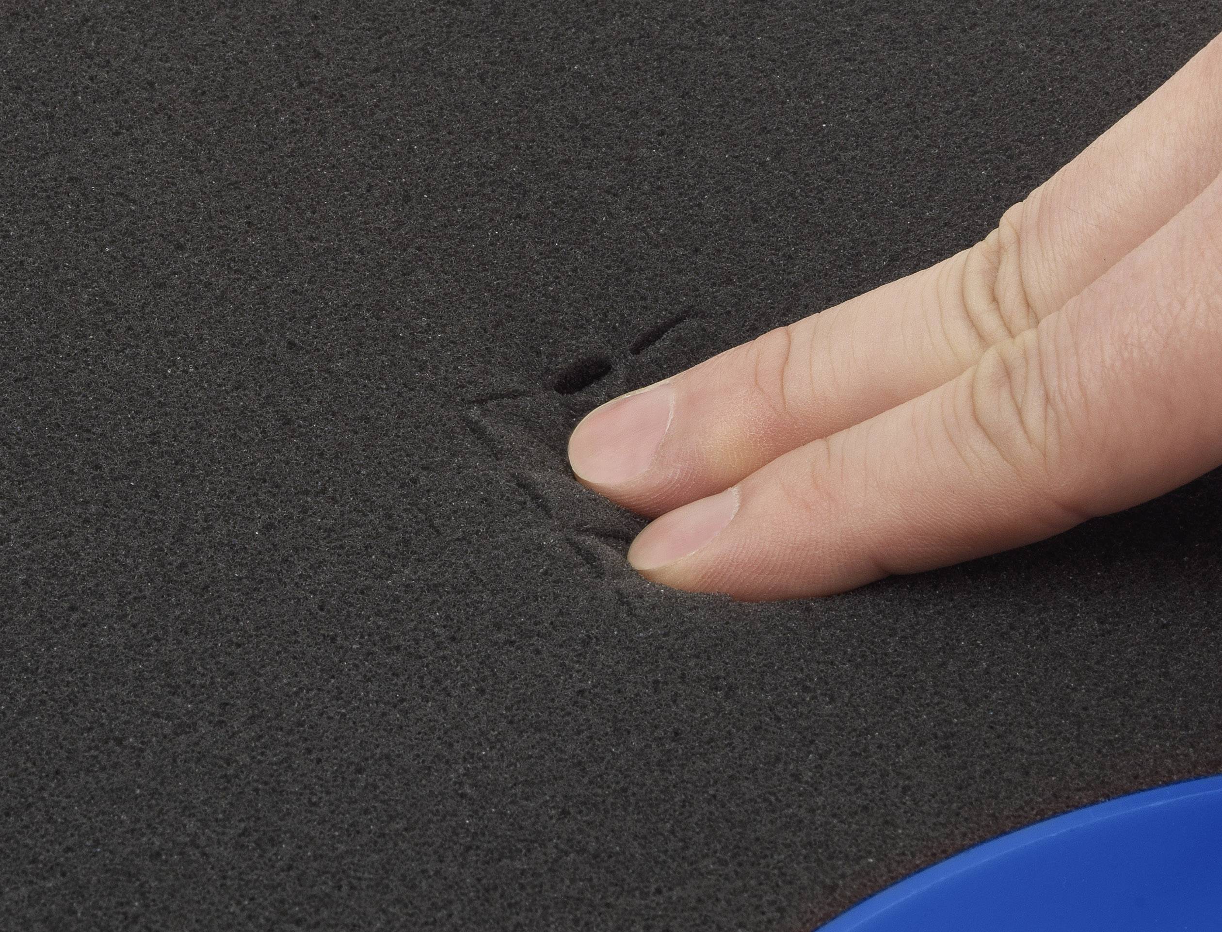 A hand presses down on black foam, visibly indenting.