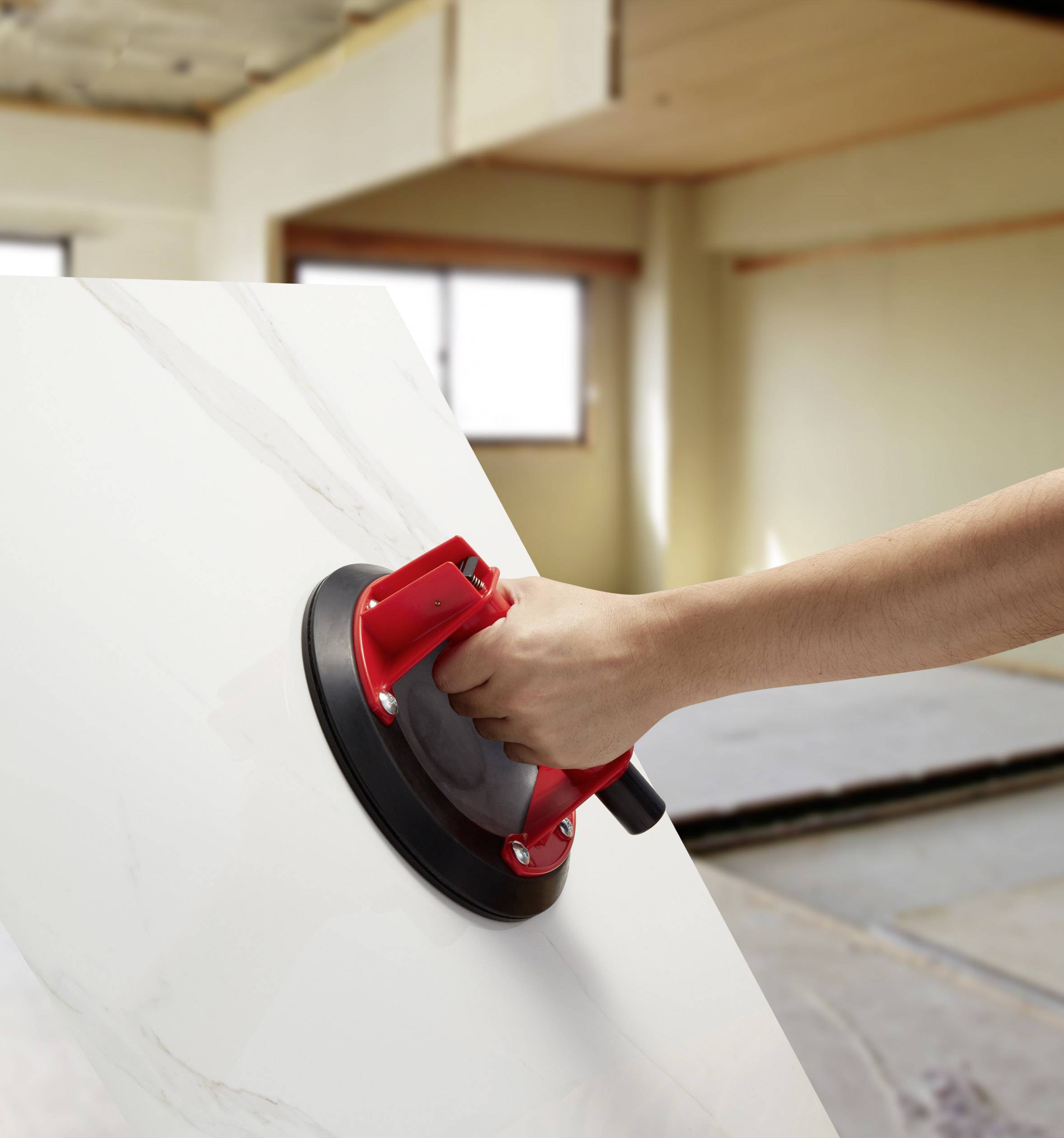 A hand is holding a red suction lifter attached to a large white panel in the renovation area.