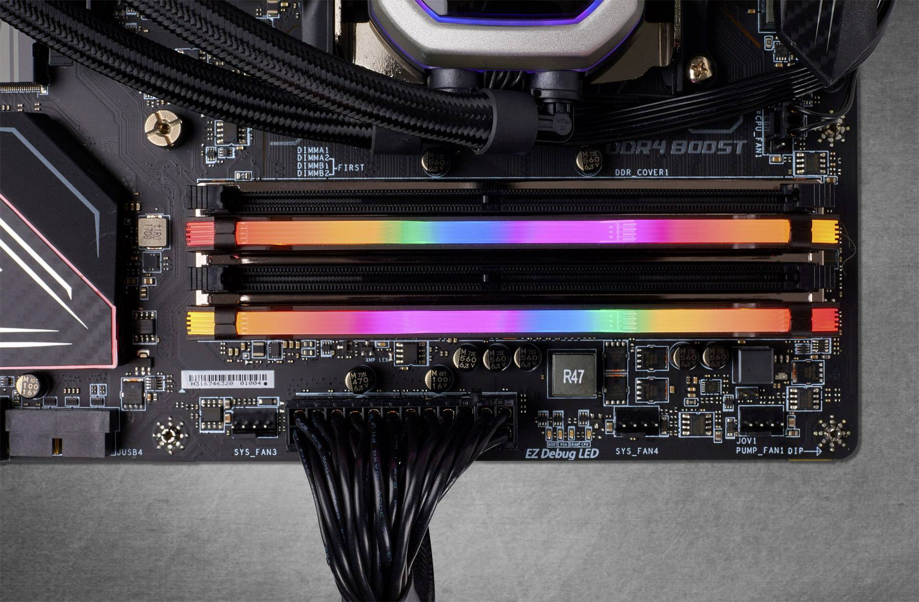 Close-up of a computer motherboard with installed RGB RAM sticks glowing in different colours. Cables are connected.