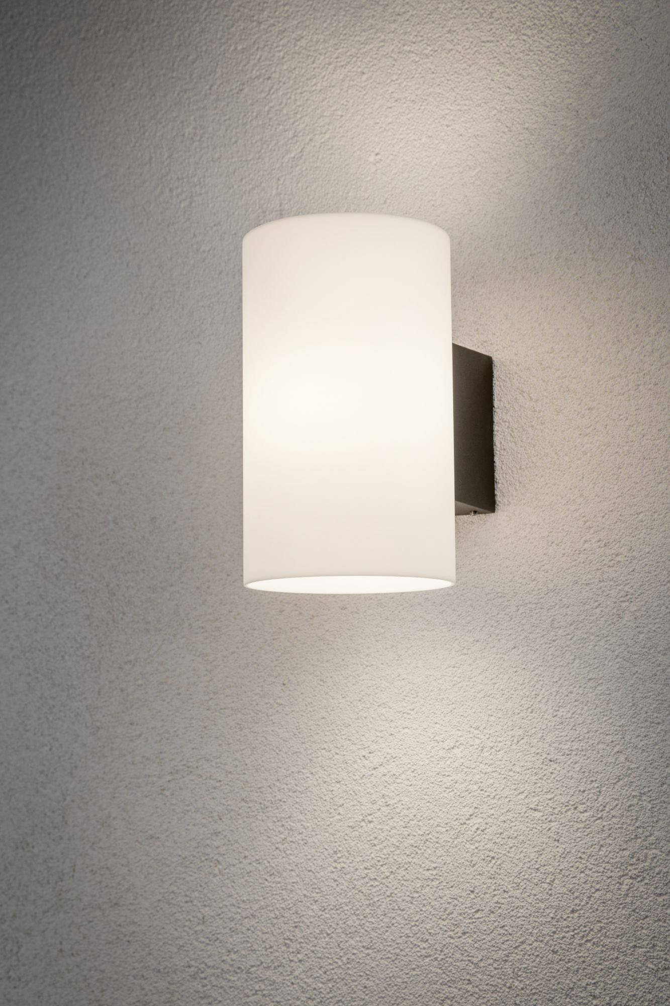 A modern, cylindrical wall light with a white shade gently illuminates a grey wall.
