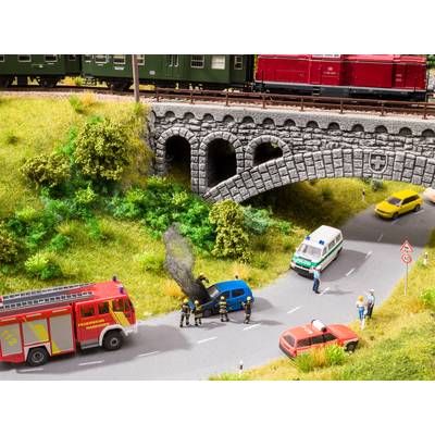 Miniature landscape depicting firefighters extinguishing a burning car on a road. A police car and an ambulance are also present at the scene.