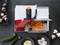 A mandolin with a red handle slices carrot rounds. On the table are courgettes, mushrooms, beetroots, and sliced potatoes.