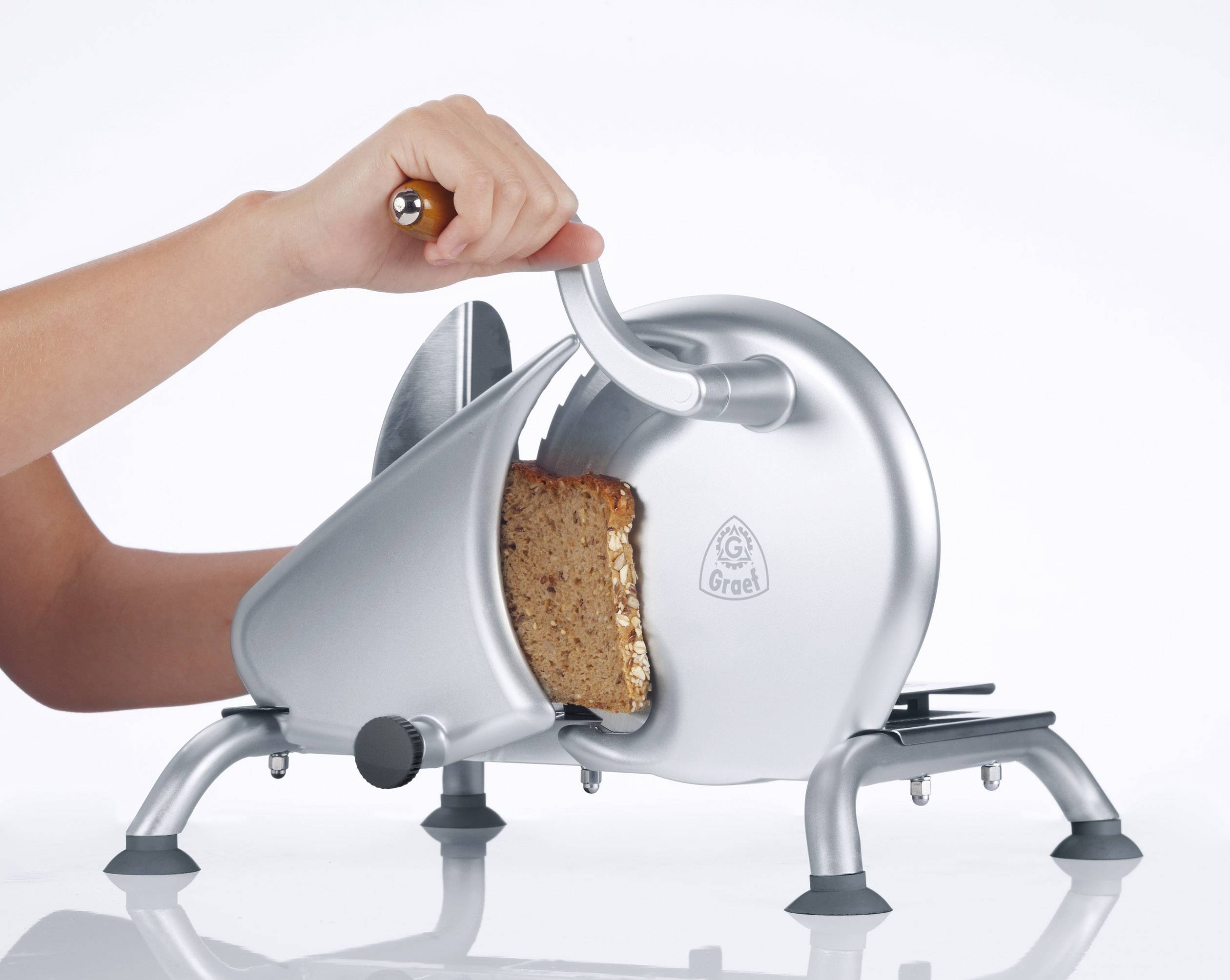 A person is slicing bread with a silver, manually operated slicer. A piece of bread is partially cut.