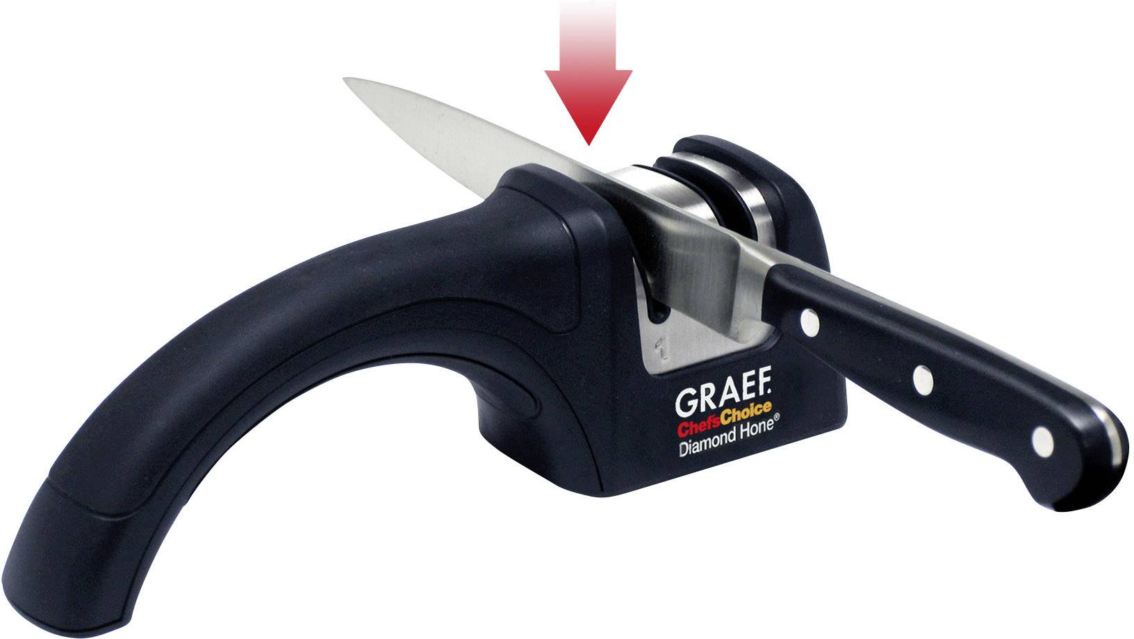 A black manual knife sharpener with a knife inserted. A red arrow above the knife indicates the sharpening direction.