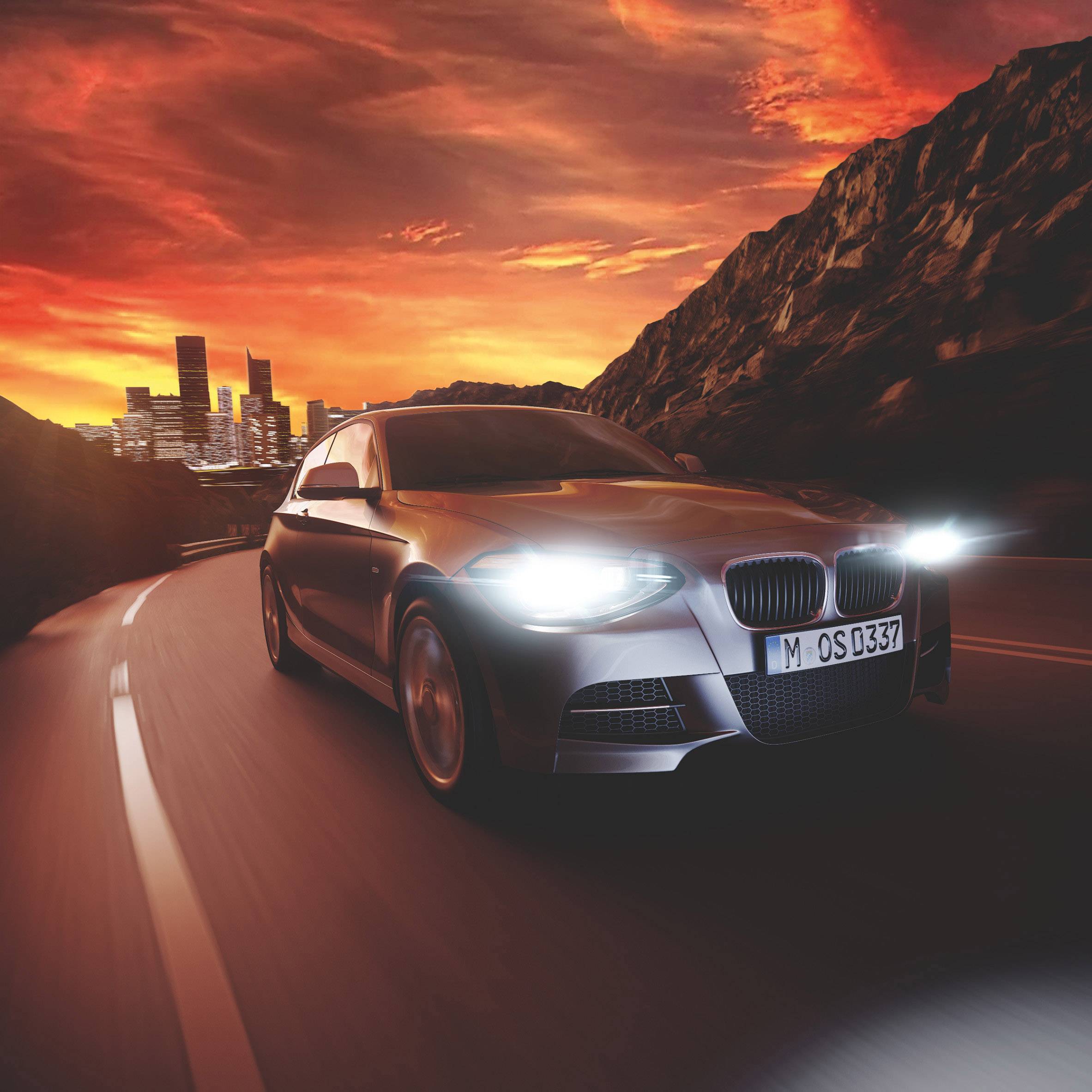 A car on a road at sunset, with a city on the horizon and mountains in the background. Scenic landscape in warm tones.
