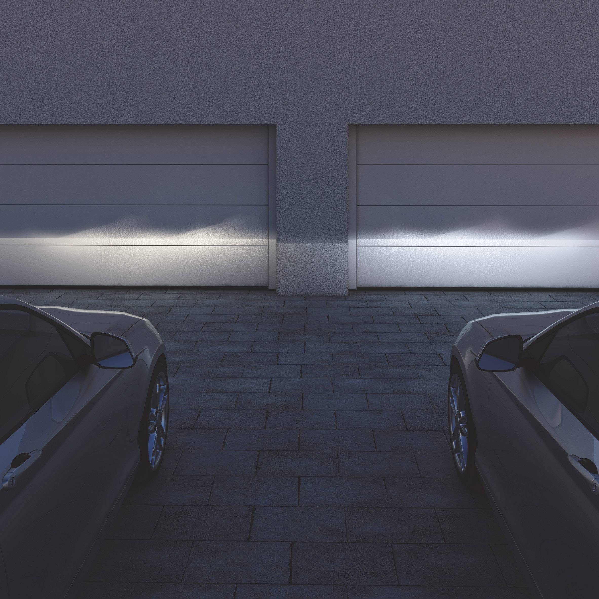 Two parked cars in front of closed garage doors under night-time lighting.