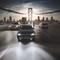 Cars drive over an illuminated bridge at sunset towards a city with a lit background. Mood: urban and dynamic.
