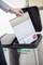 A person is placing a document into a paper recycling bin. The bin is marked with a recycling symbol and 'Recycling Paper'.