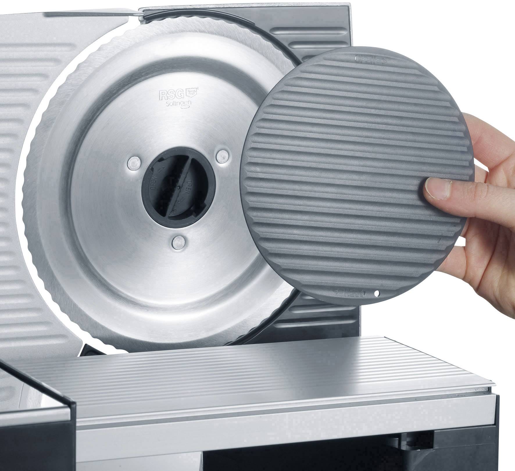 A hand is holding a round, grey protective cover that is placed in front of a metal circular saw on a kitchen cutting device.