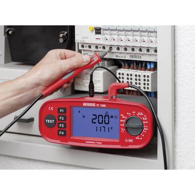 A person is using a red installation measuring device to measure the voltage in an open fuse box. The display shows '200V' and '117V'.