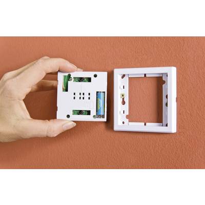 A hand holds a white light switch without its cover plate, with the cover plate positioned beside it, mounted on an orange wall.