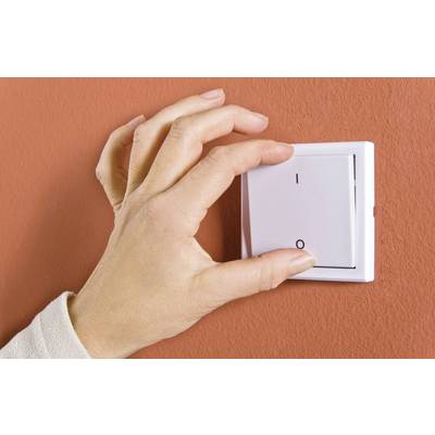 A person turns on the light switch on a red wall.