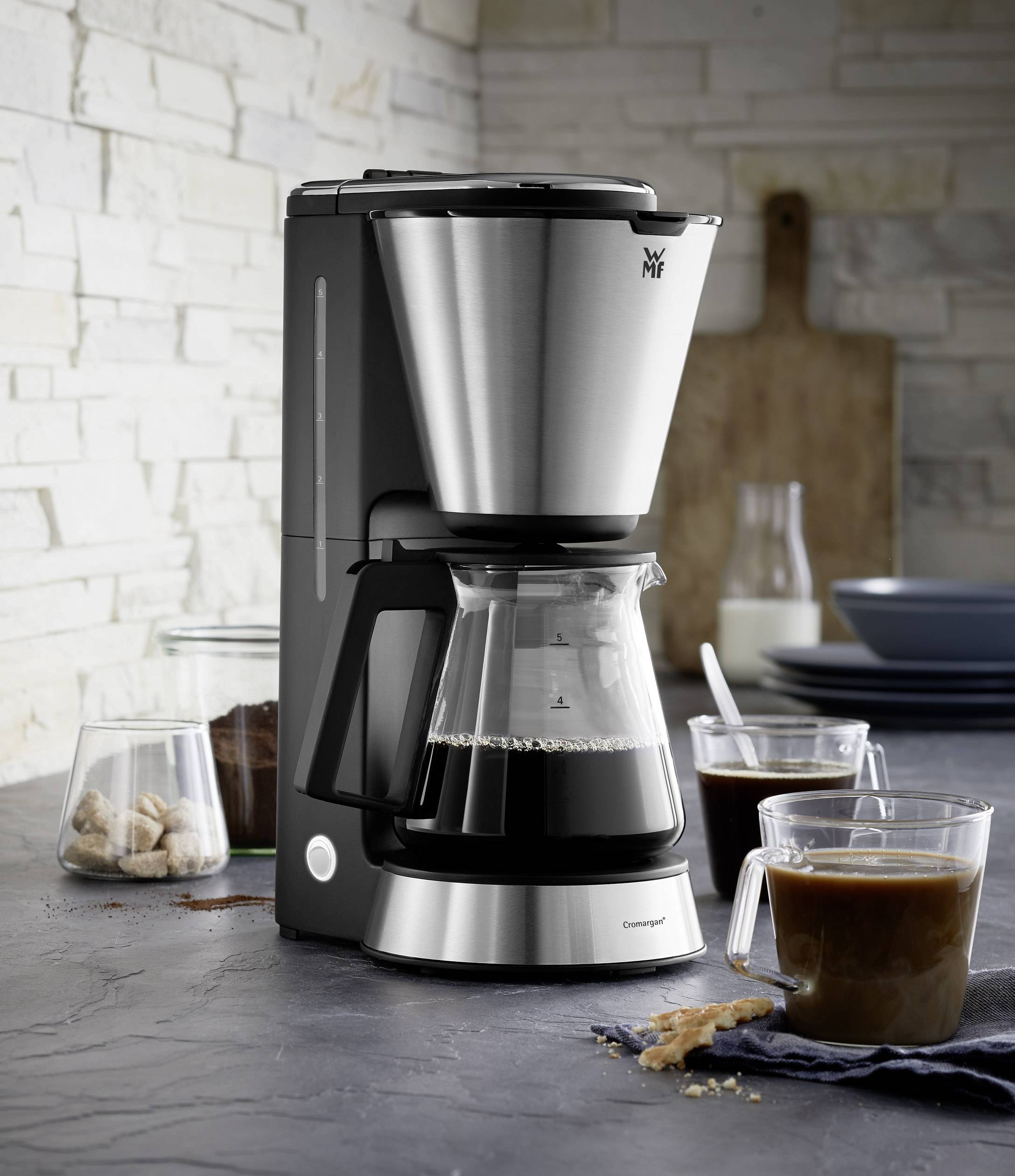 A modern filter coffee machine on a kitchen worktop. Beside it are two glasses of coffee and a glass with sugar cubes.