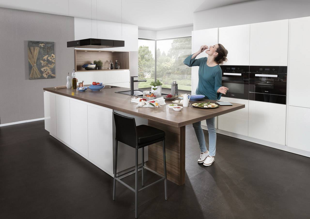 A person is standing in a modern kitchen, eating something while leaning on a large kitchen island.