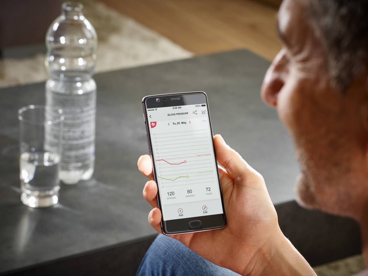 A person is holding a smartphone with a health app, displaying a graph of heart rate and blood pressure.