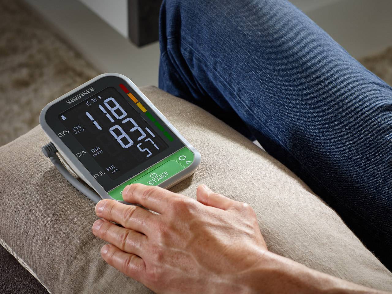 A person is measuring their blood pressure using a digital monitor. The screen displays 118 SYS, 83 DIA and 57 PULSE.