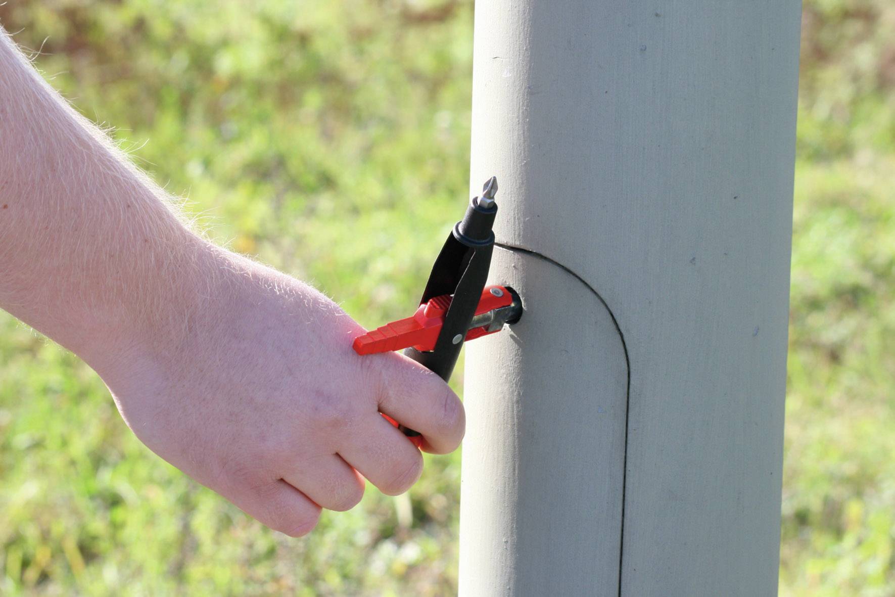 A hand is using a tool to secure a screwdriver to a metal structure outdoors.