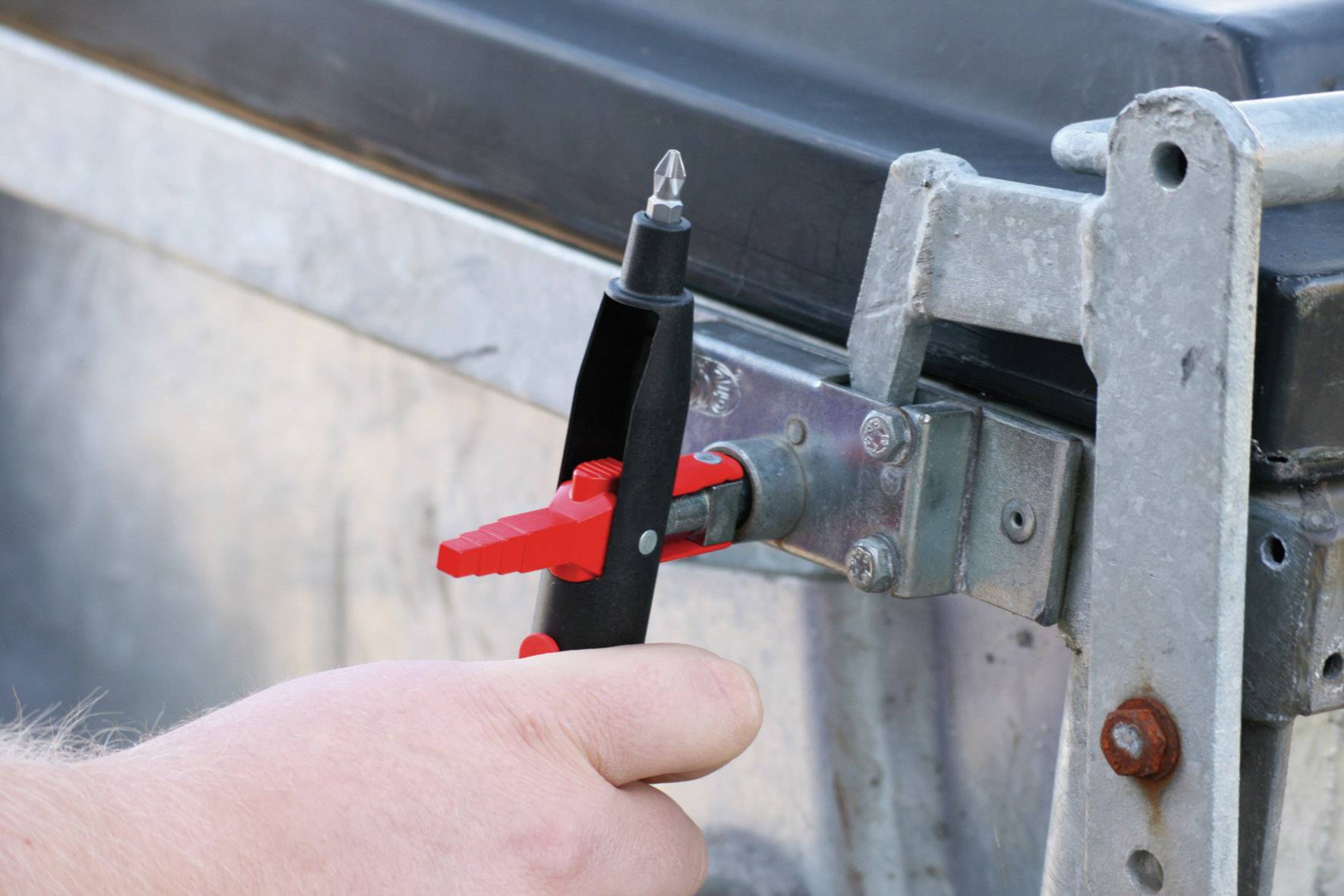 A hand is holding a security seal being applied to a metal fastener.