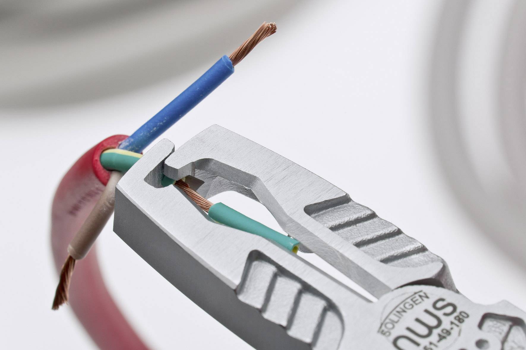 A pair of pliers removes insulation from an electrical wire; revealing blue and green cables from a red cable sheath.