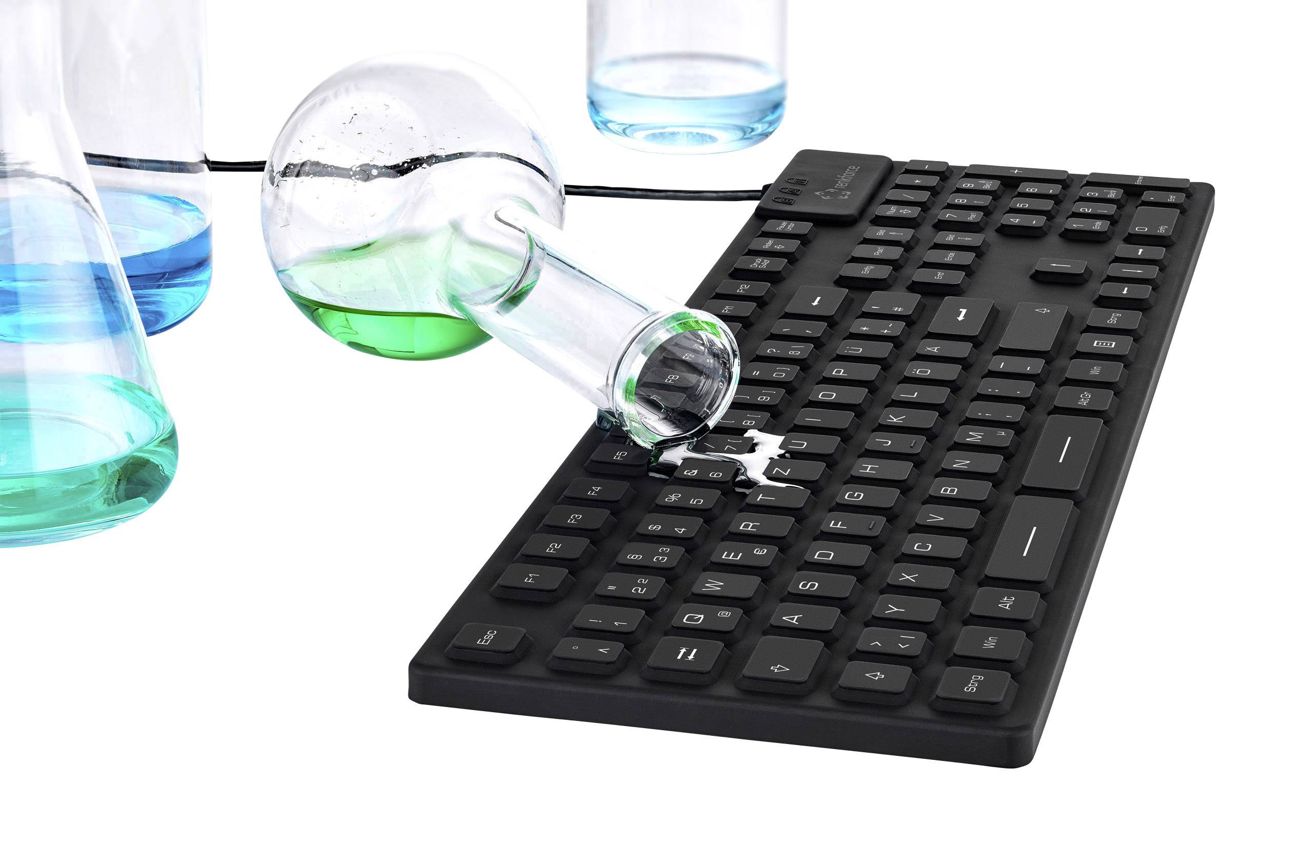 A black keyboard, onto which liquid is being spilled from an overturned test tube containing a blue-green fluid. Further glassware is visible in the background.