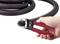 A hand is holding a red pair of pliers cutting a black, flexible pipe. A roll of the pipe is visible in the background.