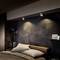 Bedroom with a modern design: Dark walls, wooden headboard, two pillows, subdued lighting, vase with branches on the left.