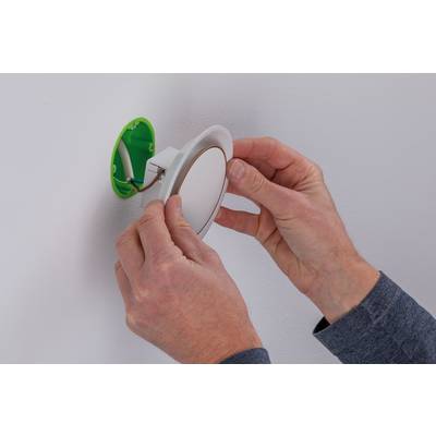 A person is installing a round LED lamp in an open green socket on a white wall.