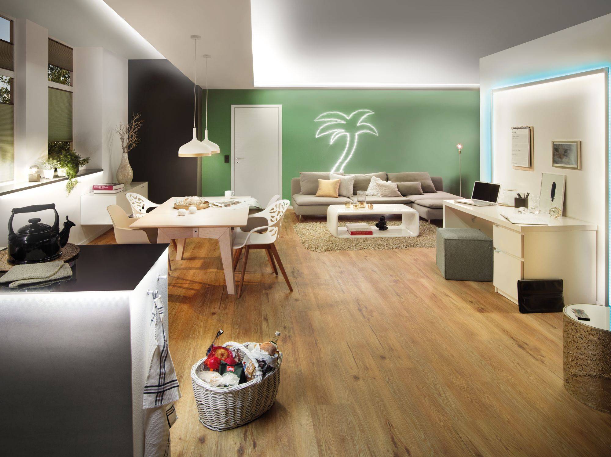 A modern living room with wooden flooring, a palm tree with green lighting against the wall, dining area to the left, sofa to the right, and a desk in the foreground.