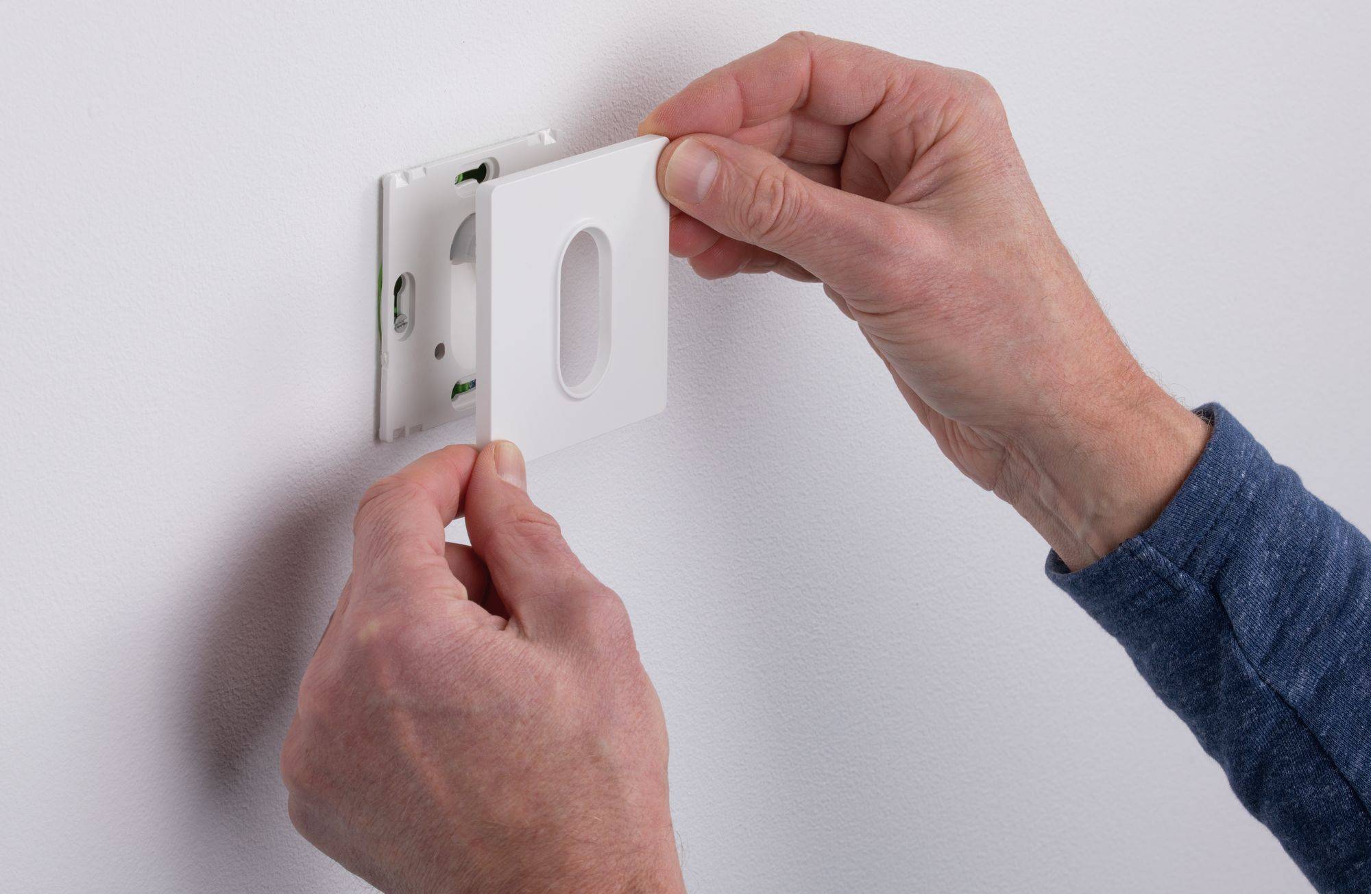 A person is installing a white cover plate on an electrical socket on a white wall.