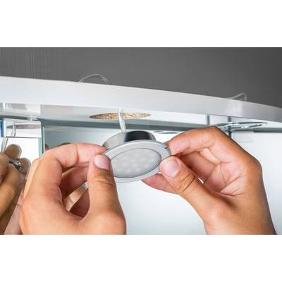 A person is installing a round, silver LED ceiling spotlight near the edge of a mirror. Hands can be seen close to the light.