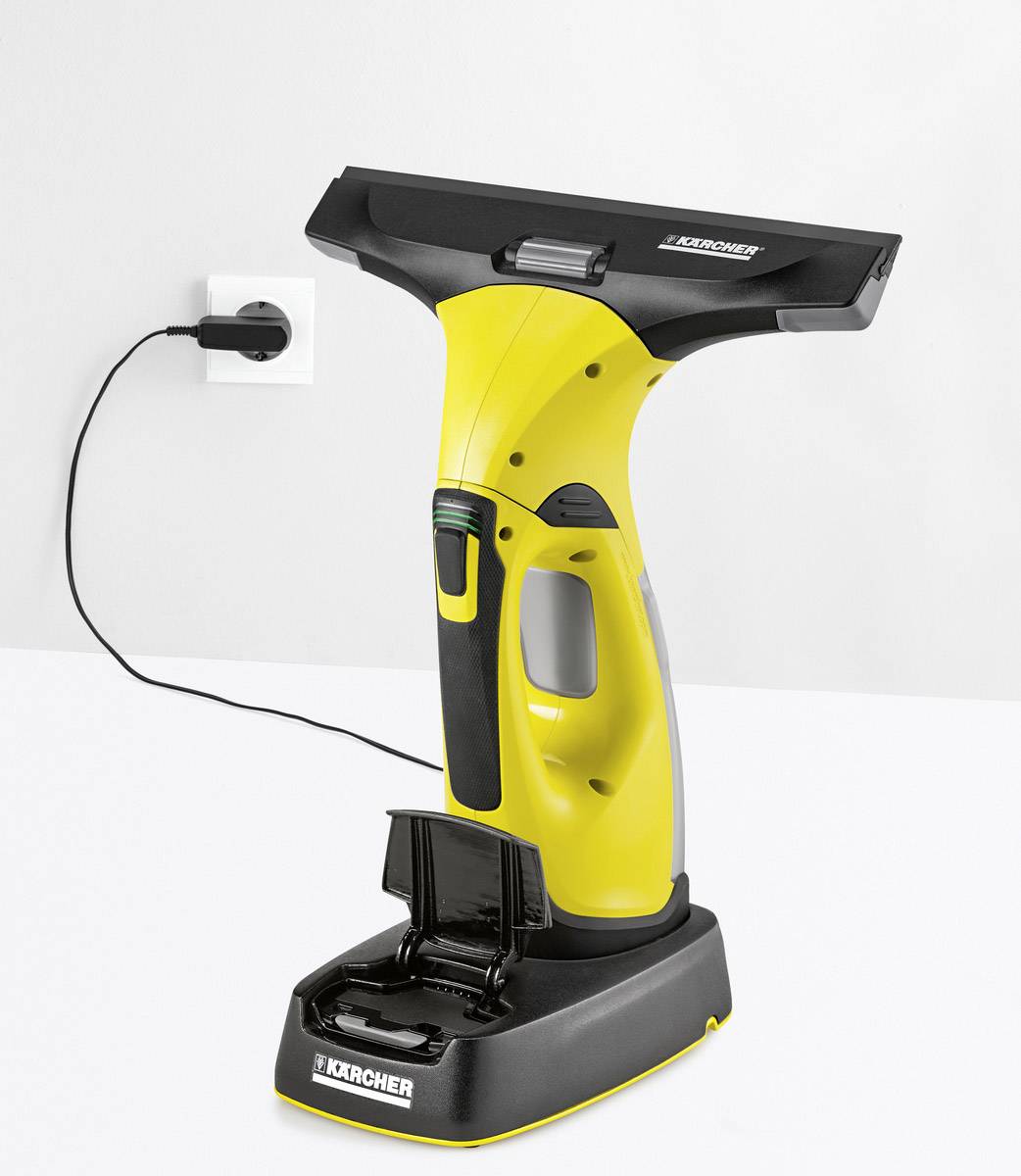 A yellow window cleaner stands on a charging station connected to a power socket. The device is ready for use.