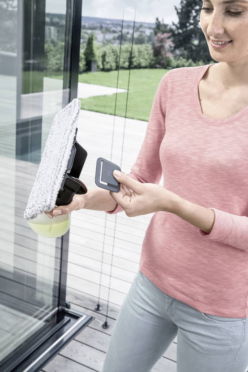A person is cleaning a large window pane with a cleaning device and soap. A garden can be seen in the background.