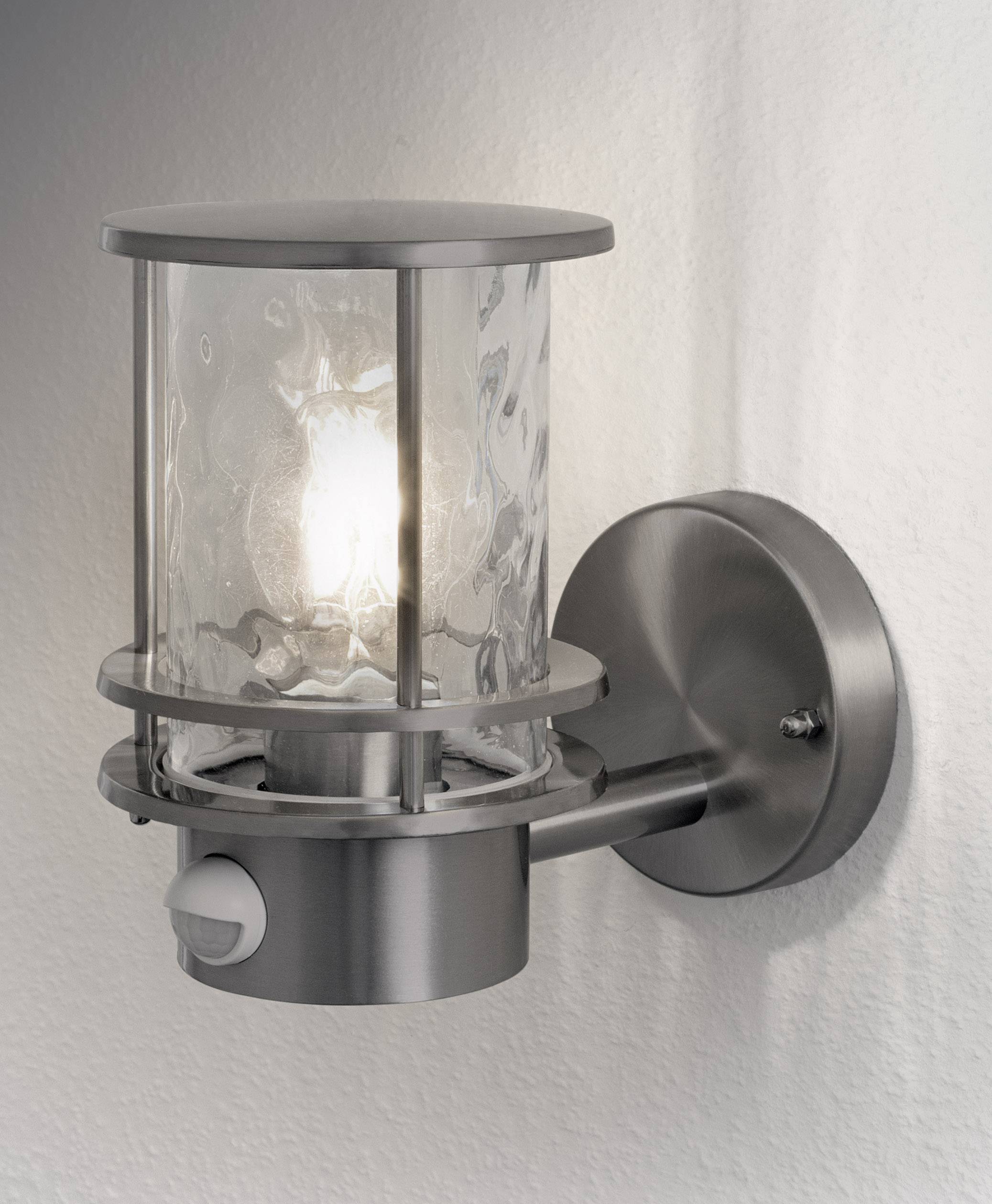 Exterior wall light made of metal with clear glass, mounted on a white wall. The light is switched on and shining brightly.