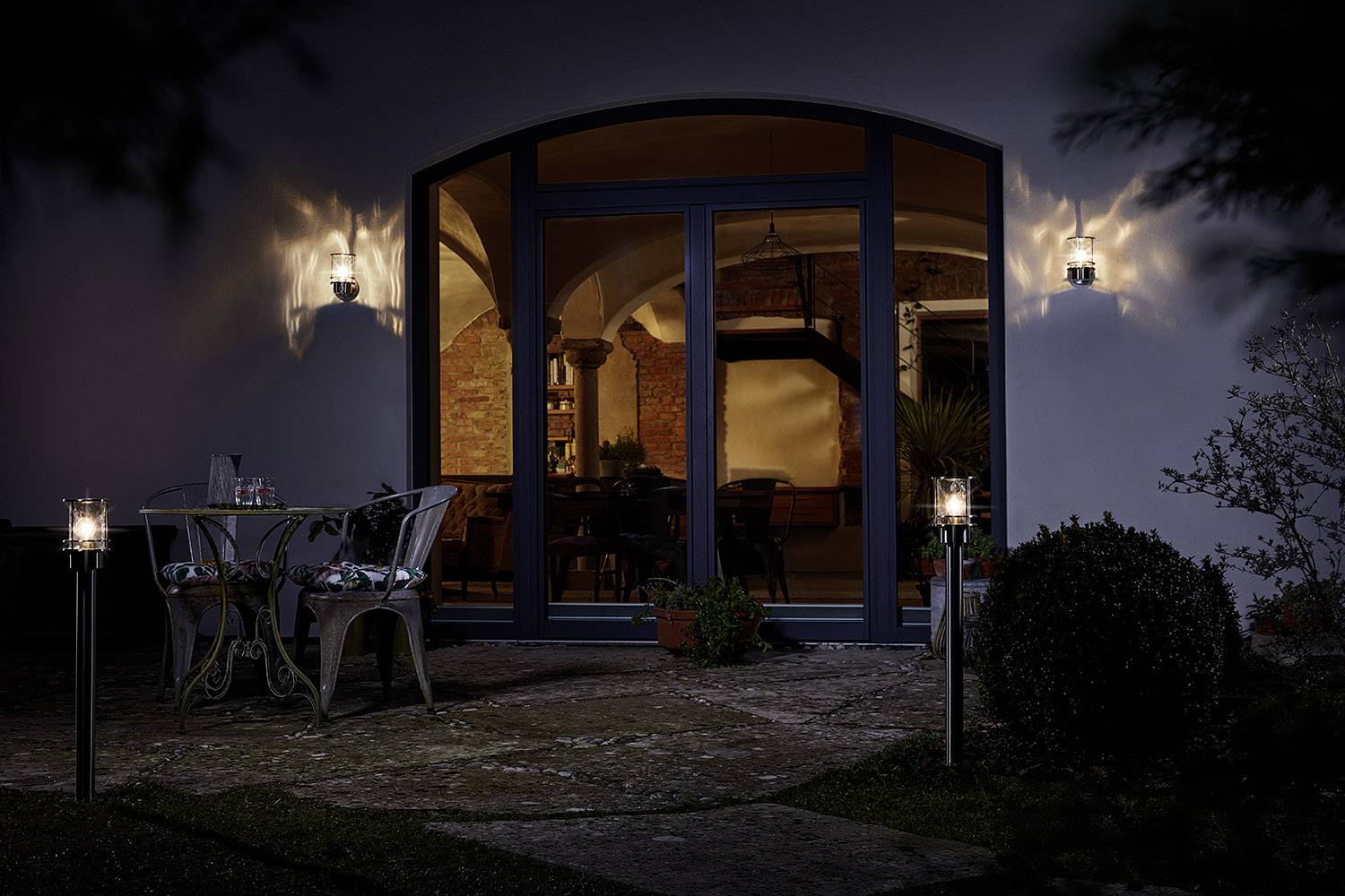 Conservatory at night with illuminated exterior area, table and chairs in the foreground, large windows revealing the interior.