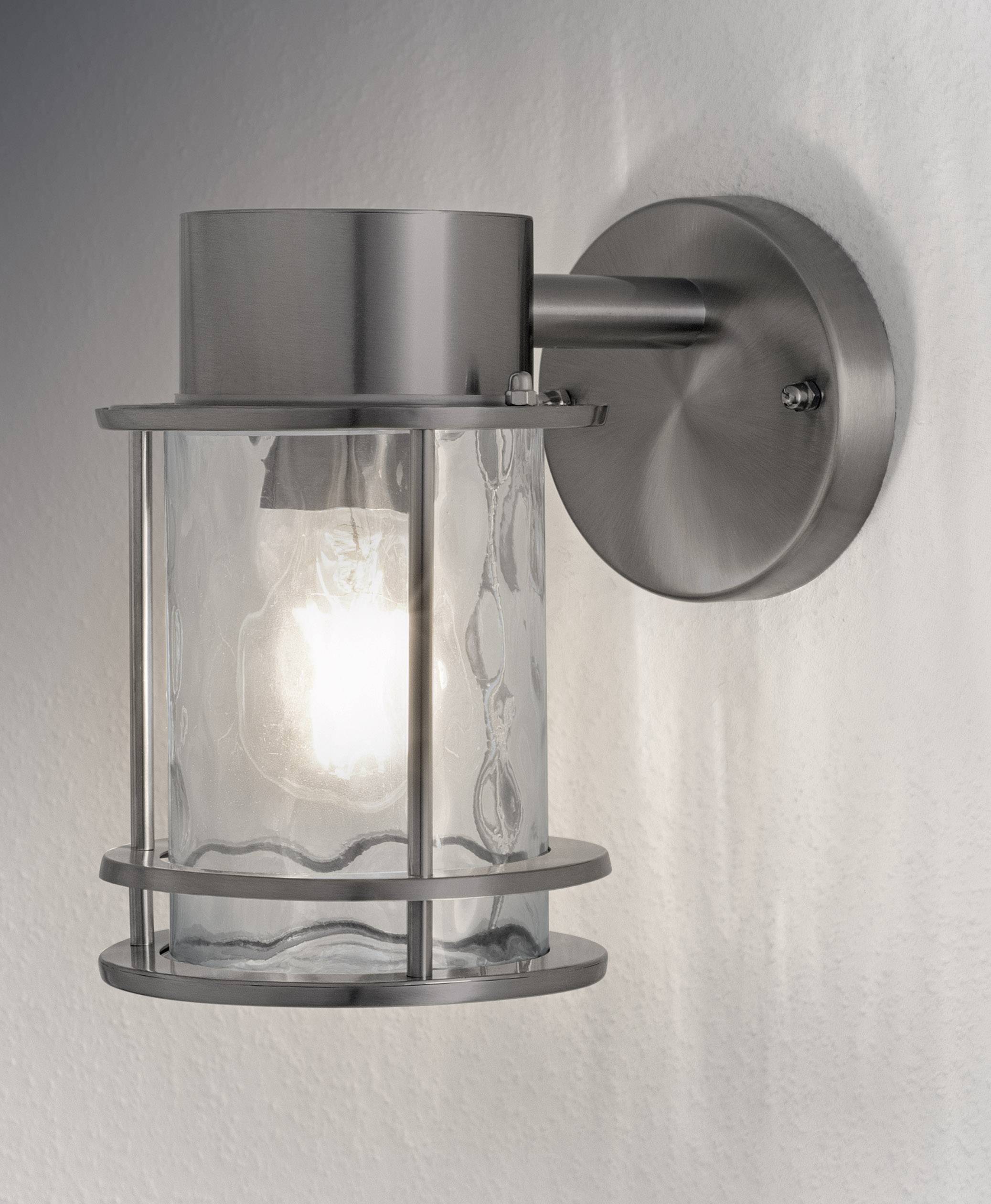 Wall light made from brushed metal with a glass housing, switched on and mounted on a wall, emitting warm light.