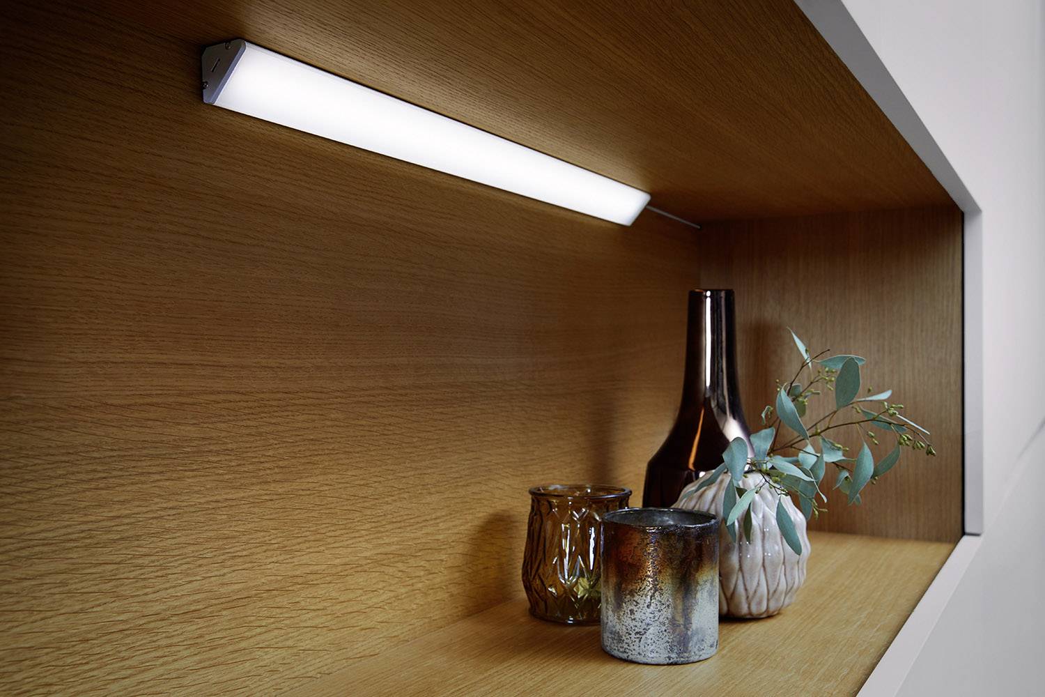 Wooden shelving unit with modern LED light; two vases are placed on it, one with a green branch, and two candleholders.