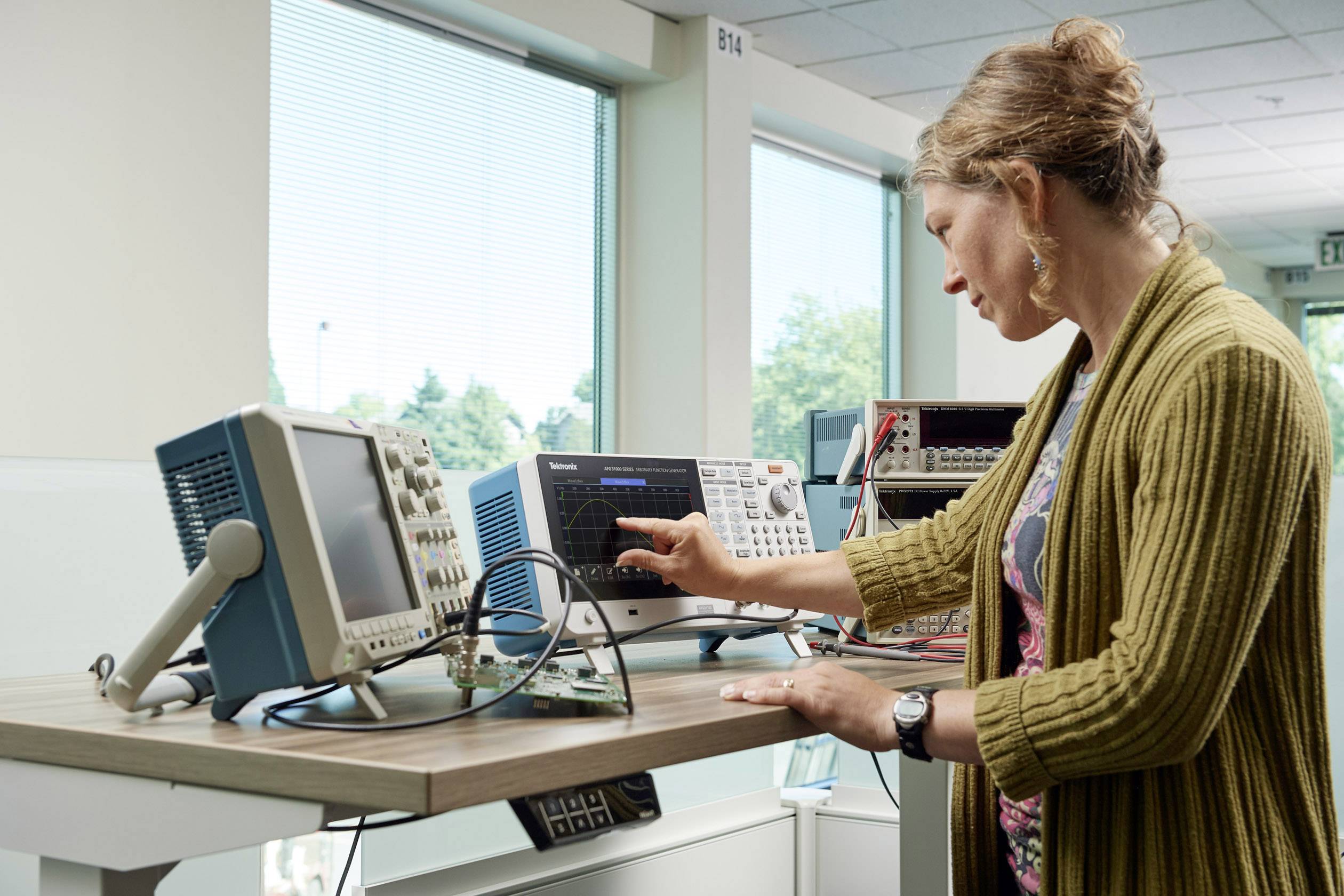 A person is working at a table with several electronic measuring devices. They are turning a knob on one of the devices to make adjustments.
