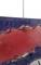 Section of a coloured drawing mounted on a wire, partially abstract with red and blue tones, suspended from a steel cable.