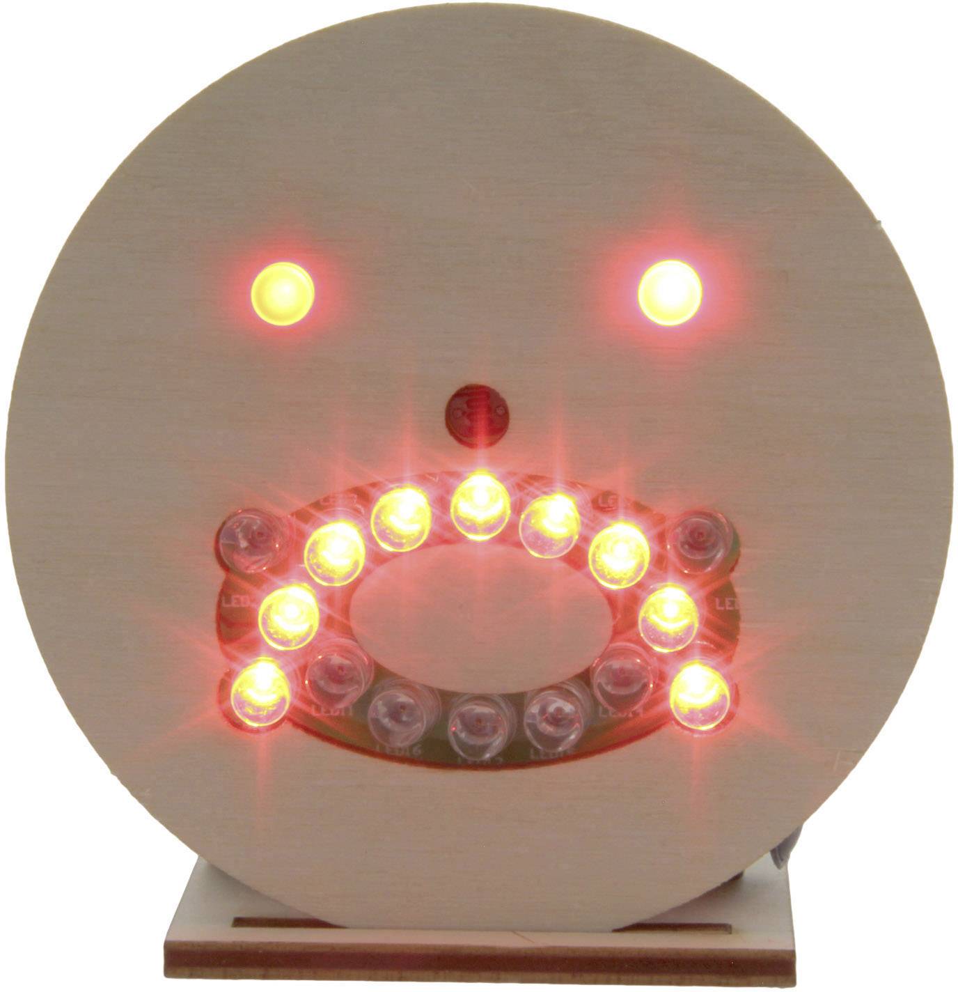 A round wooden face with glowing red LEDs forming a smiling facial expression.