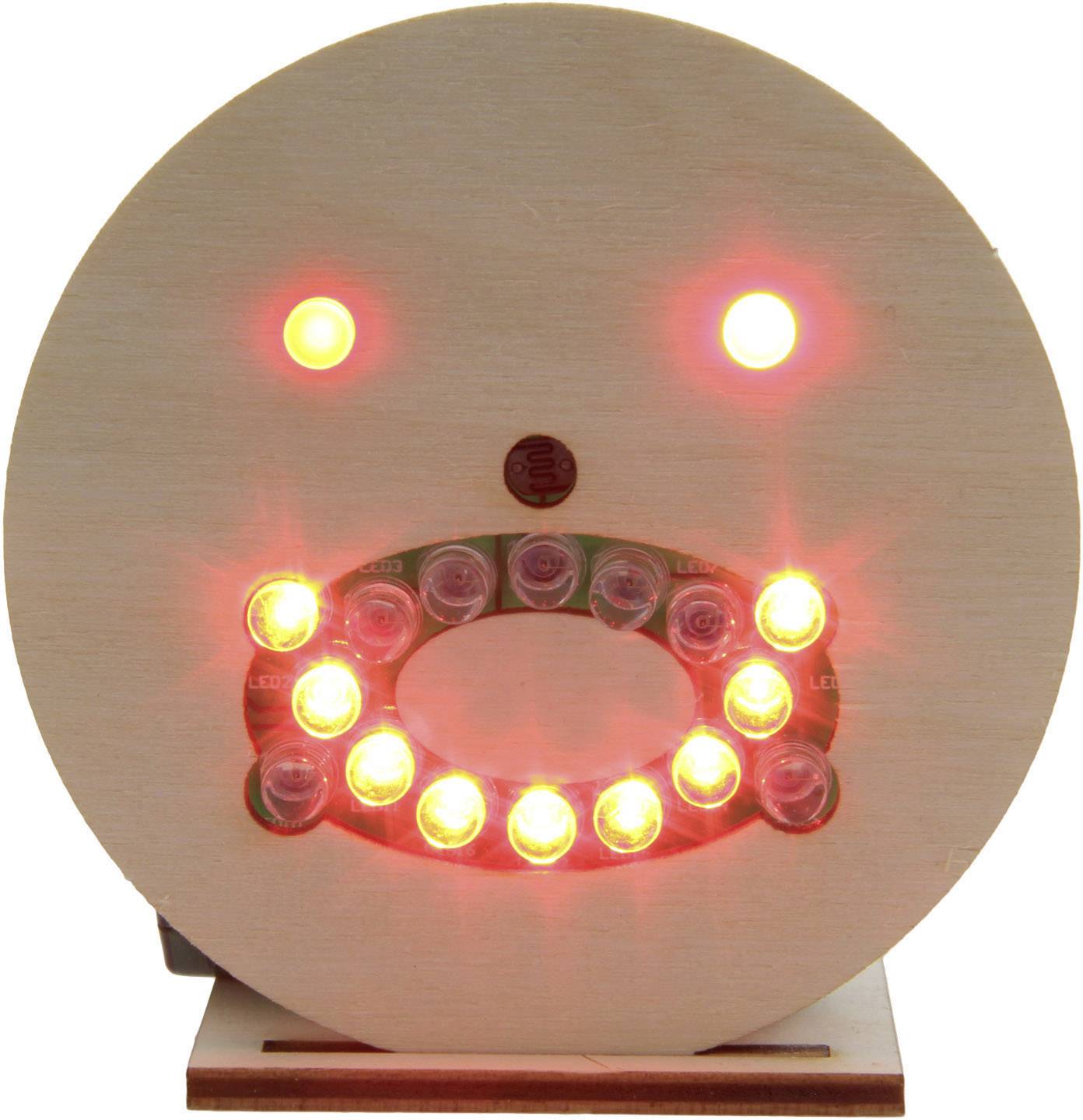 Wooden disc with illuminating red and yellow LEDs forming a smiling face.