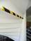 Yellow and black warning markings on the stair edge in an interior space, designed to prevent collisions. Office section visible in the background.