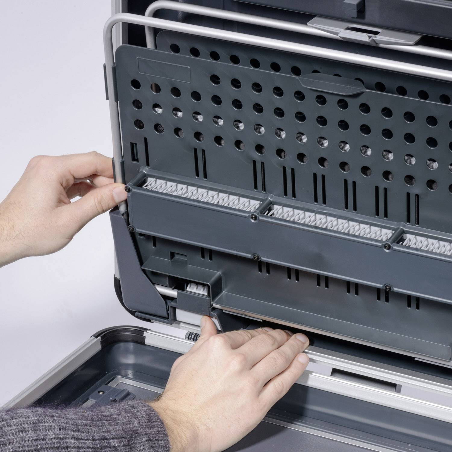 A person is installing or removing an accessory part in a dishwasher, with hands clearly visible in front of the appliance.