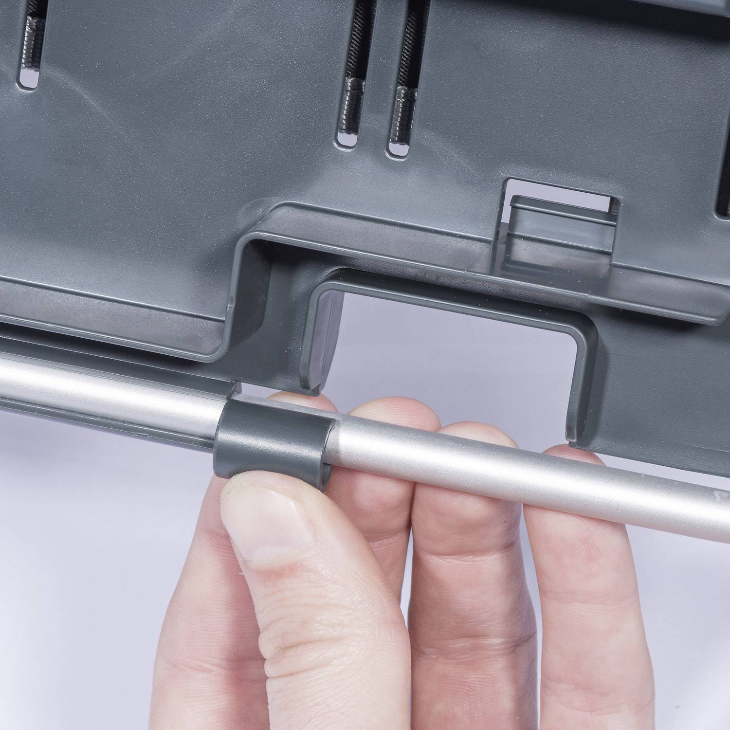 A hand holds a silver metal rod in front of a grey background with mechanical parts.
